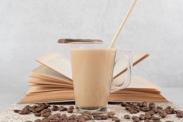 Vaso de café con chocolate, libros y granos de café sobre arpillera