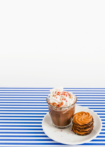 Vaso de café con crema batida y pila de galletas en un plato sobre fondo de rayas