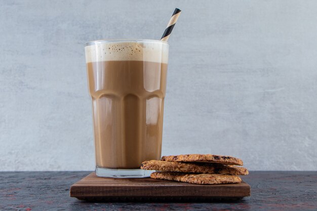 Vaso de café frío espumoso con galletas en placa de madera.