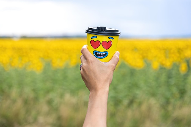 Vaso de café en una mano femenina contra el fondo de los girasoles