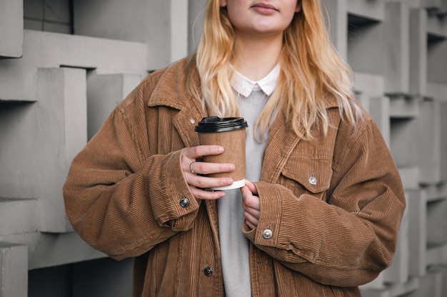 Un vaso de café en manos de una mujer con una chaqueta de pana cerrada