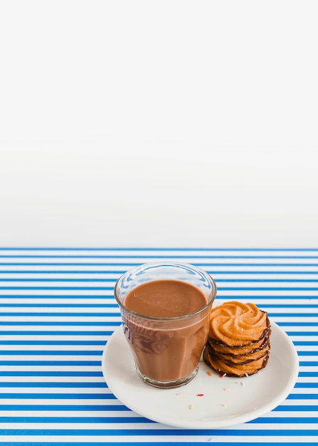 Vaso de café y pila de galletas en un plato sobre fondo blanco y rayas