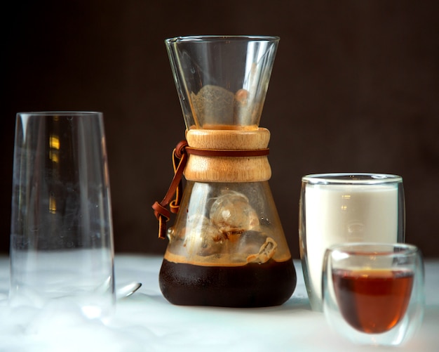 Un vaso de café en un vaso con forma única servido con leche y jarabe