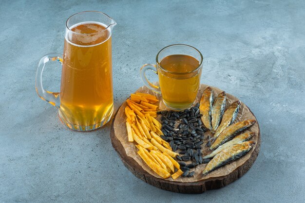 Un vaso de cerveza y aperitivos a bordo y una jarra de cerveza, sobre la mesa azul.