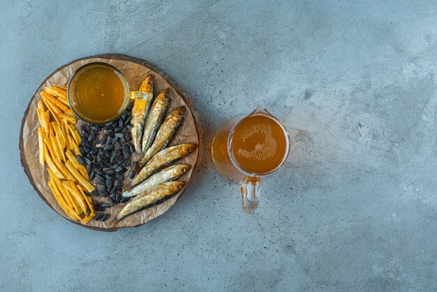 Un vaso de cerveza y aperitivos a bordo y una jarra de cerveza, sobre la mesa azul.