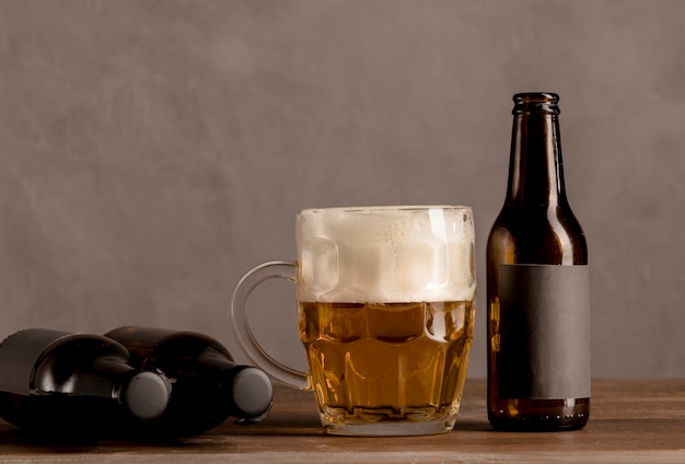 Vaso de cerveza con espuma y botellas marrones de cerveza en la mesa de madera