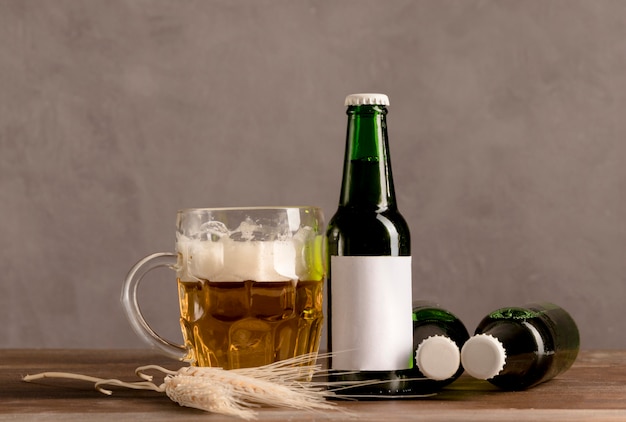 Vaso de cerveza con espuma y verdes botellas de cerveza en mesa de madera