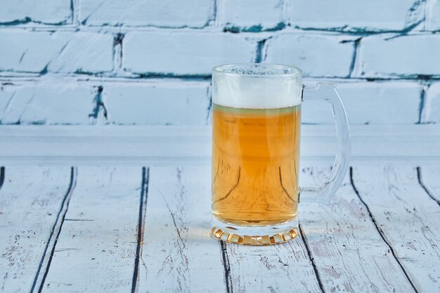 Un vaso de cerveza espumosa sobre una mesa azul.