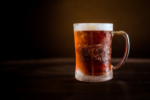 Un vaso de cerveza fría con fondo marrón oscuro