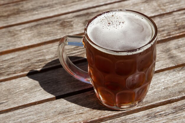 Vaso de cerveza fría sobre una superficie de madera en un día caluroso y soleado