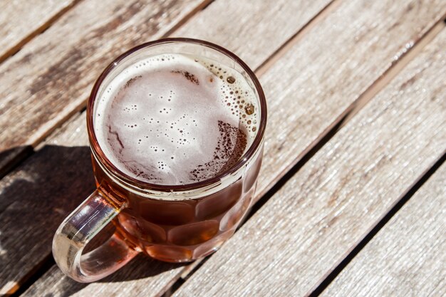 Vaso de cerveza fría sobre una superficie de madera en un día caluroso y soleado