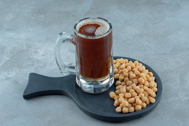 Un vaso de cerveza con guisantes sobre una tabla de cortar oscura. Foto de alta calidad