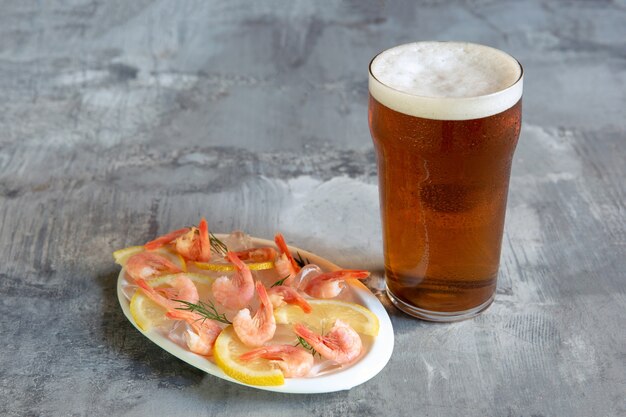 Vaso de cerveza ligera sobre fondo de piedra blanca. Se preparan bebidas alcohólicas frías y camarones con limón para la fiesta de un amigo.