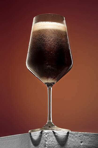 Vaso de cerveza oscura espumosa fría sobre una vieja mesa de madera