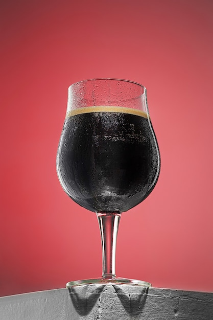 Vaso de cerveza oscura espumosa fría sobre una vieja mesa de madera