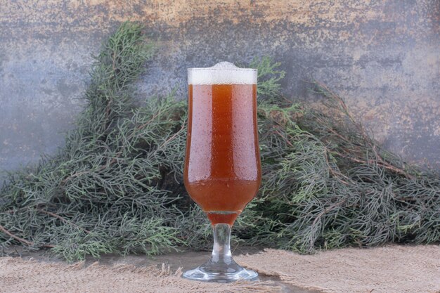 Vaso de cerveza oscura sobre arpillera con rama de pino. Foto de alta calidad