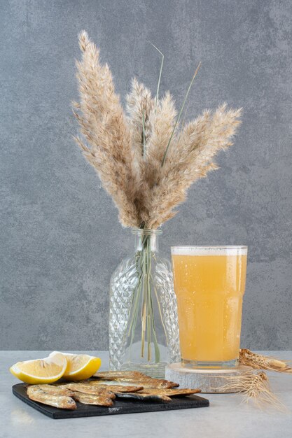 Un vaso de cerveza con pescado y rodajas de limón.