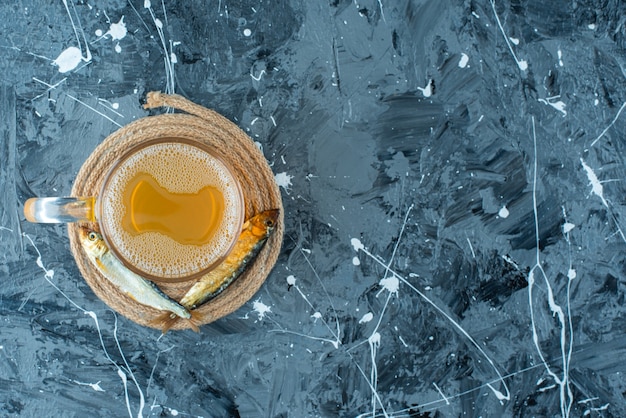 Un vaso de cerveza y pescado en un salvamanteles, sobre la mesa azul.