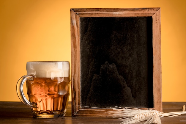 Vaso de cerveza y pizarra en mesa de madera