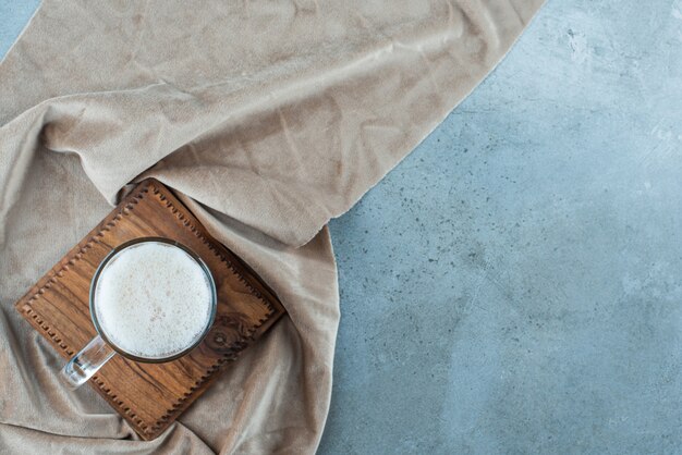 Un vaso de cerveza en una tabla sobre una toalla, sobre la mesa azul.