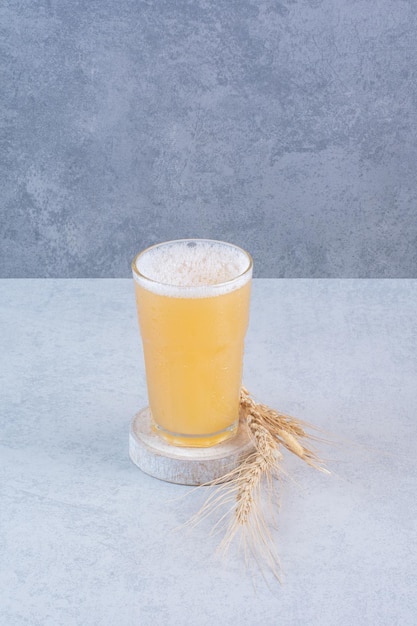Un vaso de cerveza con trigo sobre superficie blanca