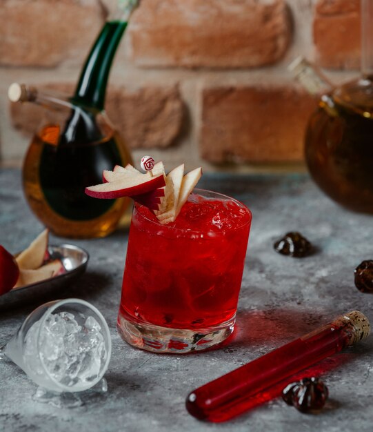 Un vaso de cóctel de alcohol rojo con rodajas de manzana y cubitos de hielo.