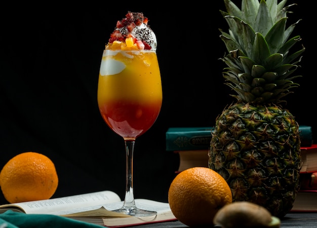 Un vaso de cóctel completo de frutas tropicales mixtas con colores vivos de pie sobre un libro deja