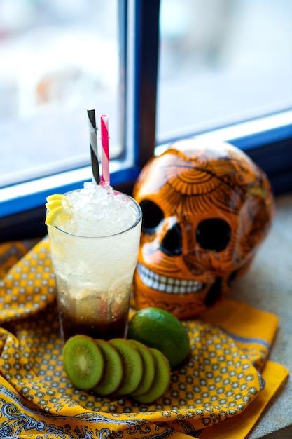 Un vaso de cóctel de lima y kiwi junto al cráneo mexicano de naranja
