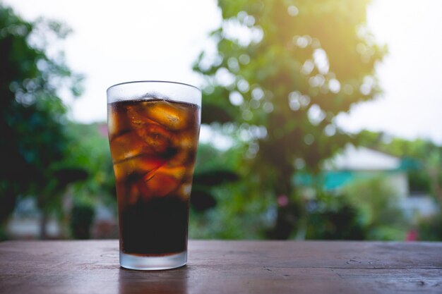 Vaso de cola con hielo en la mesa.