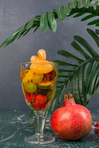 Vaso de frutas variadas y granada sobre mesa de mármol