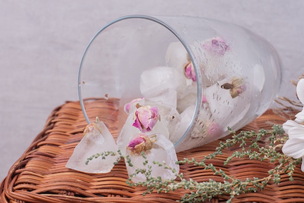 Un vaso con hielo y rosas pequeñas sobre superficie blanca