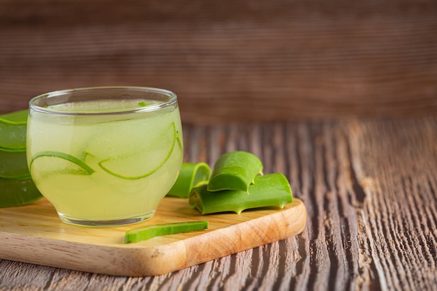 Vaso de jugo de aloe vera puesto sobre una tabla de cortar de madera