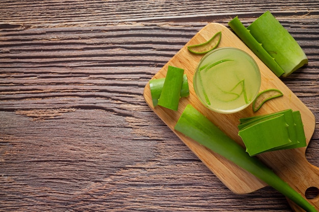 Vaso de jugo de aloe vera puesto sobre una tabla de cortar de madera