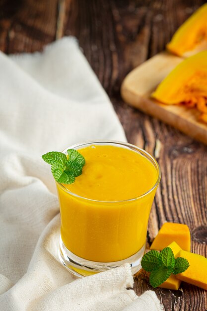 Un vaso de jugo de calabaza y calabazas crudas picadas coloque sobre un piso de madera