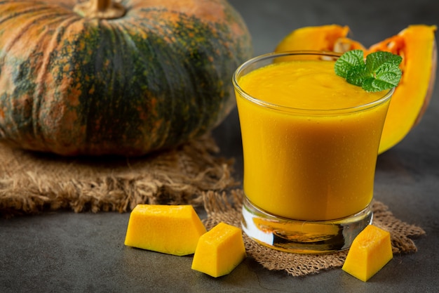 un vaso de jugo de calabaza y calabazas crudas picadas en el piso oscuro