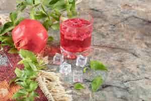 Foto gratuita vaso de jugo con cubitos de hielo y granada sobre la superficie de la piedra