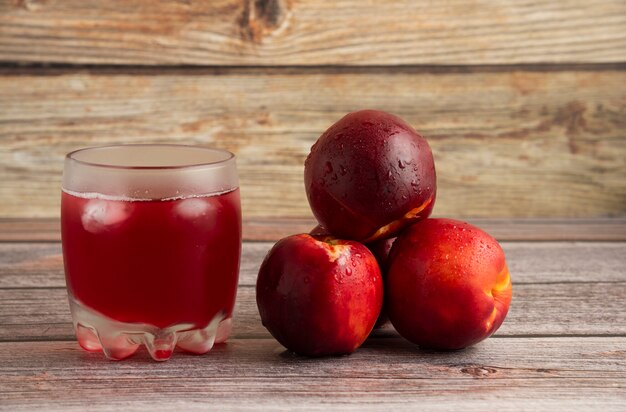 Un vaso de jugo de durazno con cubitos de hielo y fruta alrededor.