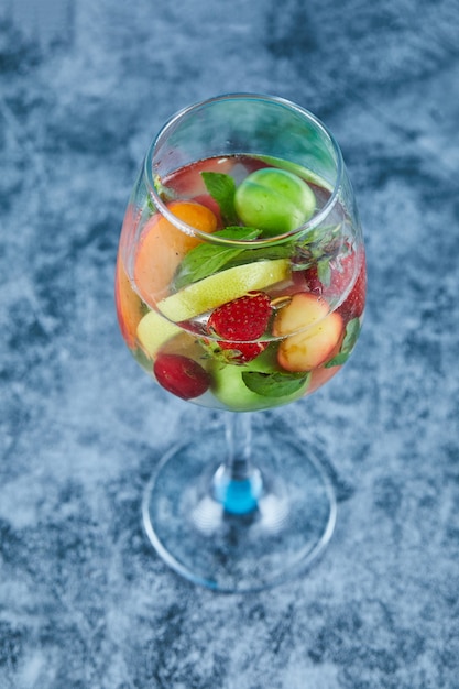 Foto gratuita un vaso de jugo con frutas enteras en el interior de la superficie azul