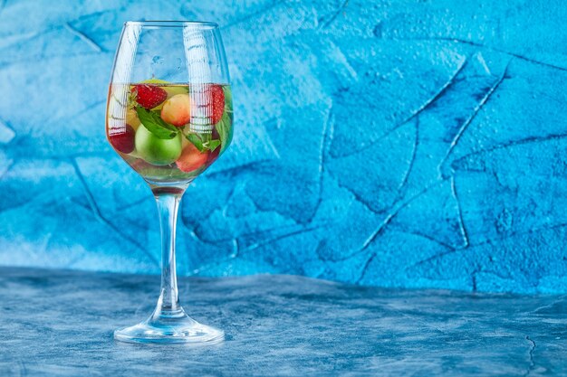 Un vaso de jugo con frutas enteras en el interior de la superficie azul