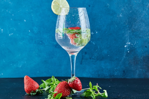 Un vaso de jugo con frutas enteras y una rodaja de limón en el interior sobre una superficie oscura