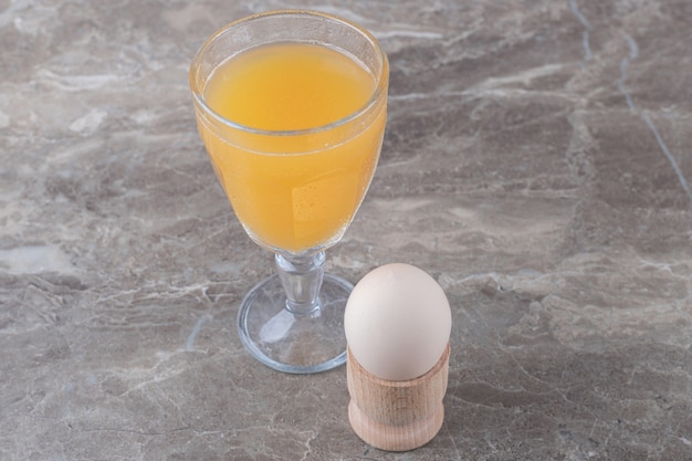 Vaso de jugo y huevo en mesa de mármol.