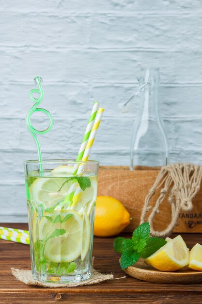 Un vaso de jugo de limón con caja de madera y cuerda sobre superficie de madera y blanca, vista lateral. copiar espacio para texto