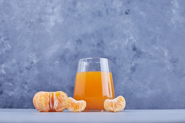 Un vaso de jugo de mandarina con frutas alrededor.