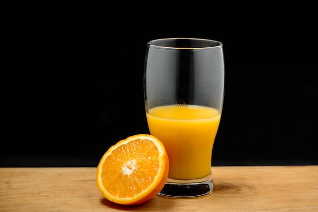 Vaso de jugo y media naranja en escritorio de madera