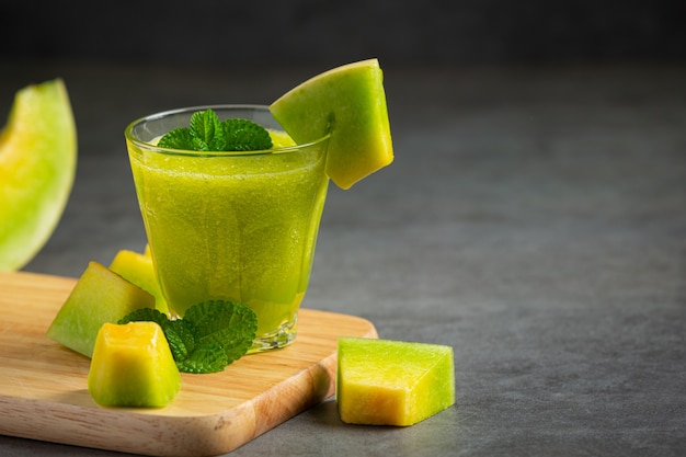 Vaso de jugo de melón puesto sobre tabla de cortar de madera