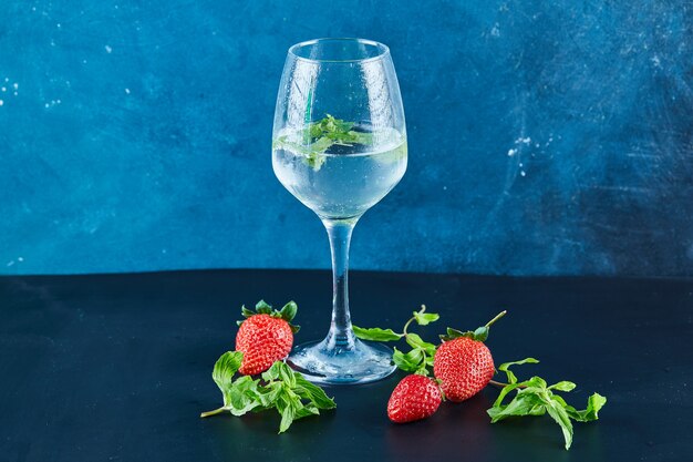 Un vaso de jugo con menta y fresas frescas y menta sobre superficie azul