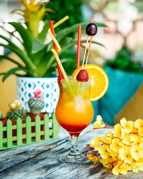 Un vaso de jugo de naranja adornado con fresa, rodaja de naranja y cereza.