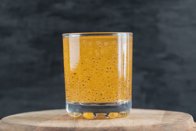 Un vaso de jugo de naranja amarillo sobre negro sobre un trozo de tabla de madera