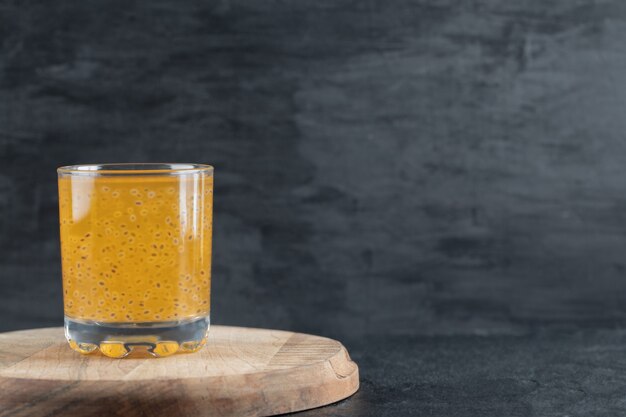 Un vaso de jugo de naranja amarillo sobre negro sobre un trozo de tabla de madera