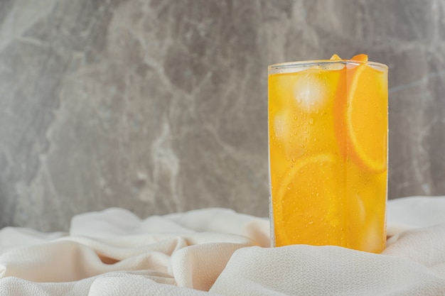 Foto gratuita un vaso de jugo de naranja con cubitos de hielo sobre tela de satén